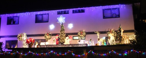 A festive display of Christmas lights, featuring a decorated tree, snowflakes, and various holiday decorations on a building.