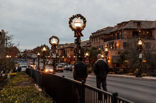 A festive street scene with decorated lamp posts, people walking, and buildings adorned for the holiday season.