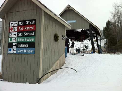 A ski resort building with signs for ski patrol, school, and tubing, surrounded by snow and ski lifts in the background.