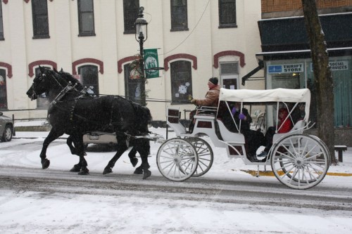A horse-drawn carriage travels through a snowy street, with passengers enjoying the winter scenery.