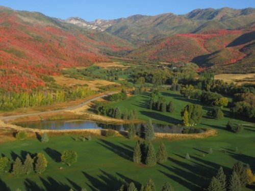 Aerial view of a vibrant landscape with rolling hills, colorful autumn foliage, a pond, and lush green fields.