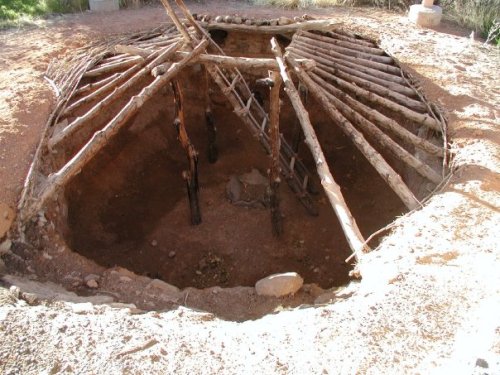An underground structure with wooden beams and a circular opening, surrounded by earth and rocks.