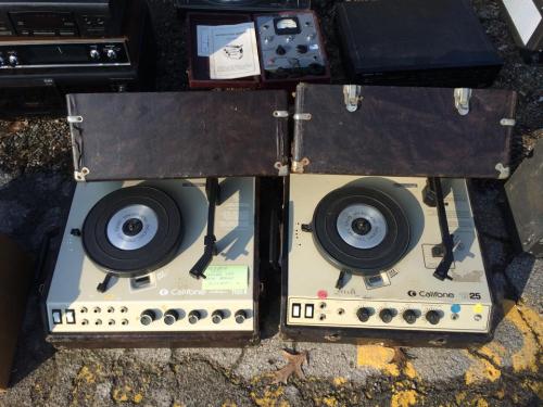 Two vintage turntables with open lids, placed on a surface among other retro audio equipment.