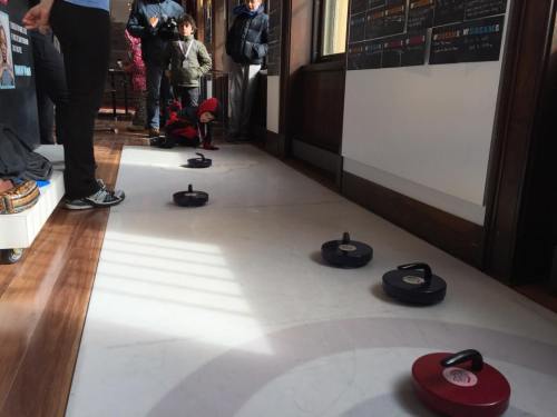 A curling rink with stones on the ice, while spectators watch from the side.