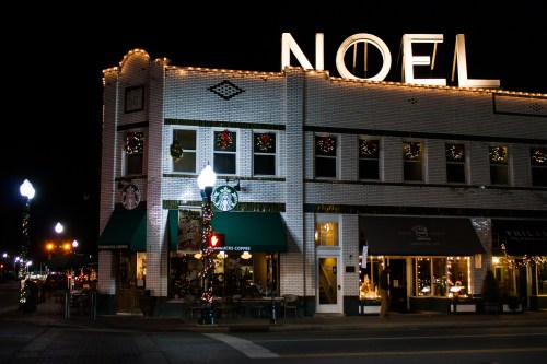 A festive building at night, adorned with holiday lights and decorations, featuring a Starbucks on the ground floor.