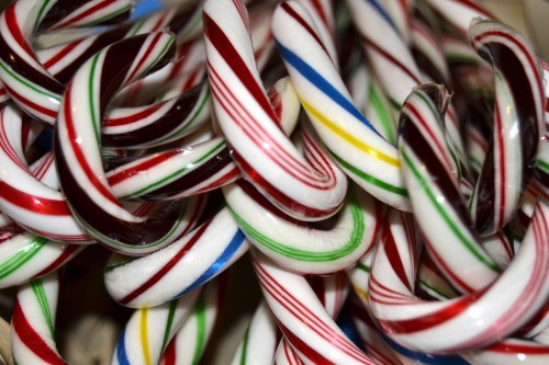 A close-up of colorful candy canes twisted together, featuring red, white, green, yellow, and blue stripes.