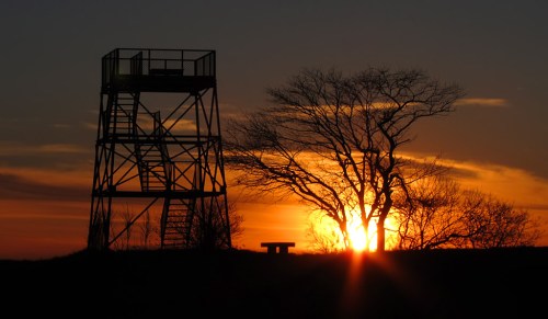 Silhouette of a watchtower and a tree against a vibrant sunset sky.