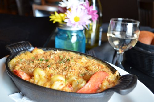 A baked pasta dish in a cast iron skillet, topped with breadcrumbs, alongside a glass of white wine and flowers in a jar.