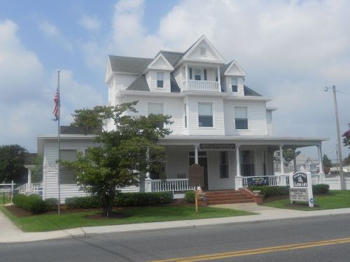 A large white Victorian-style house with multiple gables, a porch, and an American flag in front.
