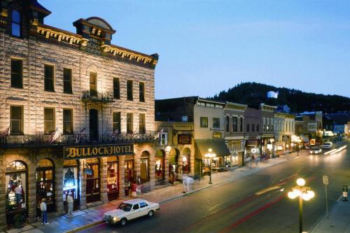 Historic buildings line a street at dusk, featuring the illuminated Bullock Hotel and charming storefronts.