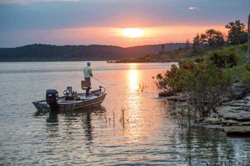 A person fishing from a small boat at sunset, with calm waters and a scenic landscape in the background.