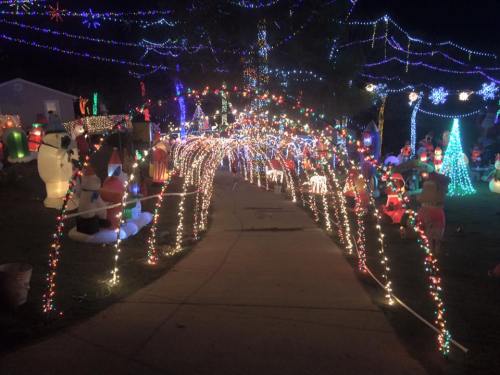 A festive pathway illuminated with colorful holiday lights and decorations, creating a cheerful atmosphere at night.
