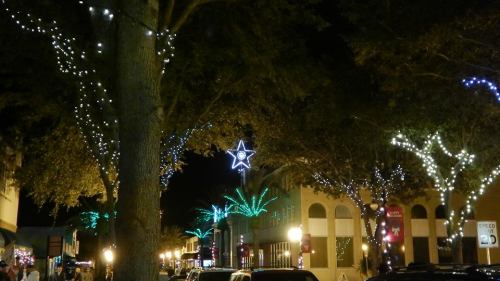 A festive street scene at night, adorned with colorful lights and a star hanging among illuminated trees.