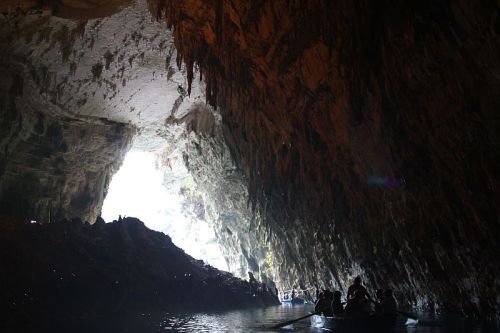 A dark cave with a bright opening in the distance, featuring silhouettes of people in a boat.