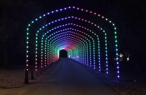 A colorful light tunnel arching over a dark road, creating a festive and inviting atmosphere at night.
