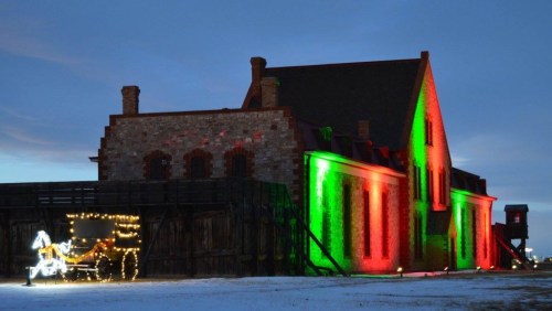 A historic building illuminated with red and green lights, featuring a decorative horse-drawn carriage nearby.