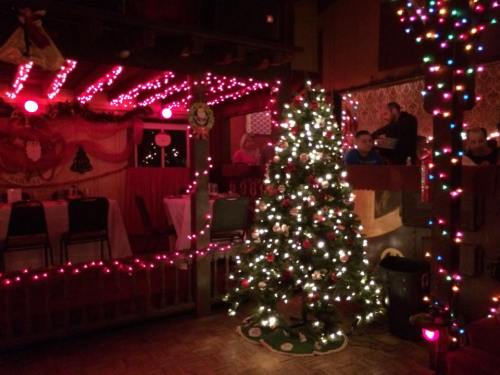 A cozy room decorated for Christmas with a lit tree, colorful lights, and festive table settings.