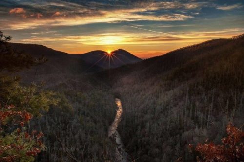 A stunning sunset over a valley, with mountains framing a winding river below and colorful clouds in the sky.