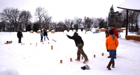 A group of people playing a game in the snow, with wooden blocks set up in a snowy landscape.