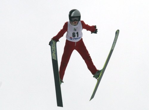 A skier in a red suit performs a jump in mid-air, wearing a helmet and number 61 on their chest.