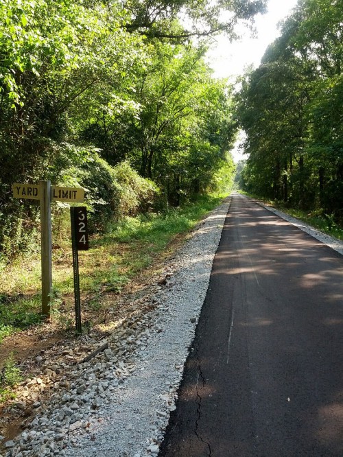 A tree-lined path with a yard limit sign and a marker reading "324" along a newly paved road.