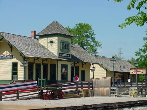 Historic train station with a yellow exterior, tower, and decorative elements, surrounded by greenery and a wooden platform.