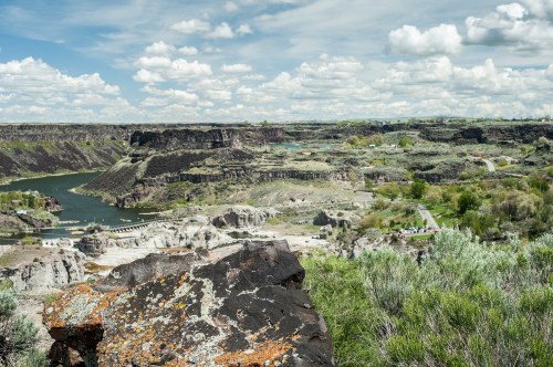 A scenic view of a canyon with a river, lush greenery, and cloudy skies in the background.