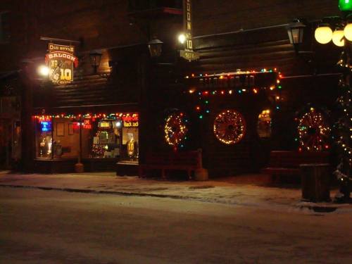 A cozy building decorated with colorful holiday lights, featuring a snowy street and festive wreaths on the windows.