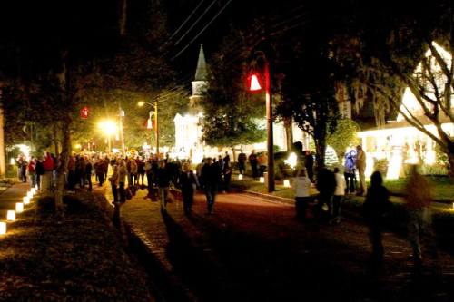 A lively street scene at night, with people walking among festive lights and decorations.