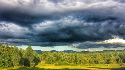 Dramatic clouds loom over a lush green landscape with distant mountains under a moody sky.