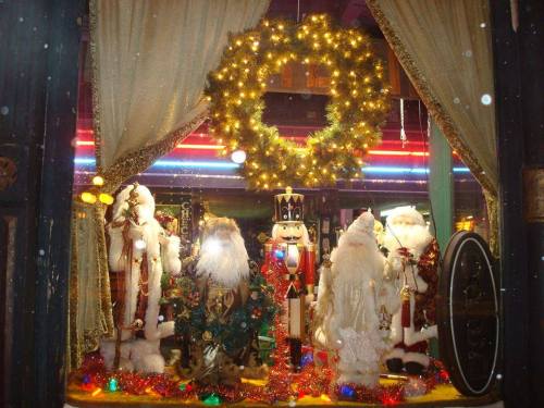 A festive window display featuring Santa figures, a nutcracker, and a decorated wreath with colorful lights.