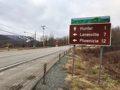 Road sign indicating directions to Hunter (1 mile), Lanesville (7 miles), and Phoenicia (12 miles) near a mountain.