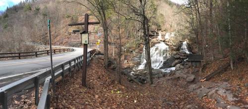A scenic view of a waterfall beside a road, surrounded by trees and autumn leaves.