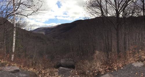 Panoramic view of a valley surrounded by mountains, with bare trees and scattered clouds in the sky.