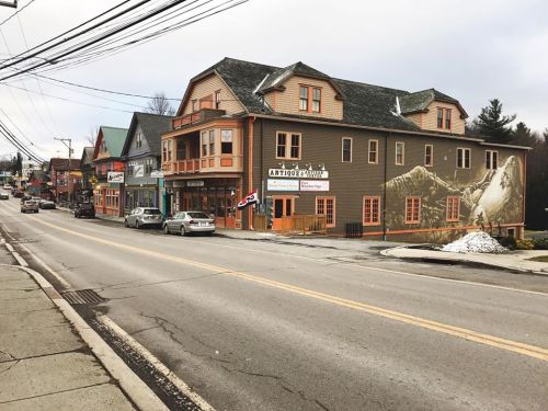 A street view of a quaint town with shops and a large building featuring a mountain mural. Snow is visible on the ground.