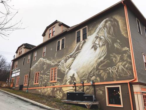A large mural of a mountain scene on the side of a brown building with orange trim and windows.