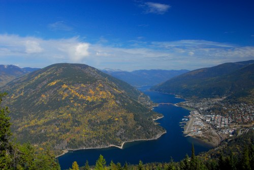 A scenic view of mountains and a river, with a small town nestled at the water's edge under a blue sky.