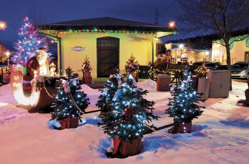 A festive scene with decorated Christmas trees, lights, and a Santa figure outside a building in a snowy setting.