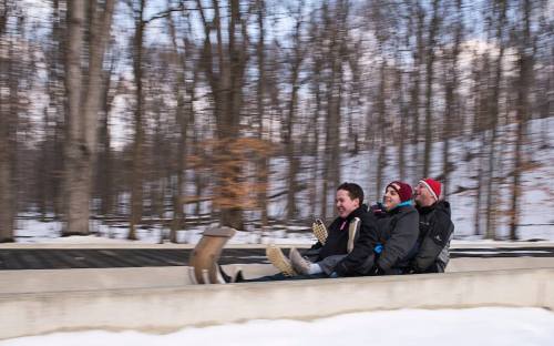 Three friends slide down a snowy hill on a sled, laughing and enjoying the winter scenery around them.