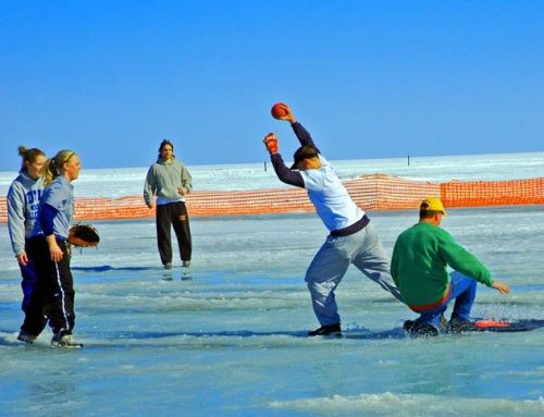 A group of people playing on ice, with one person sliding while others watch and prepare to throw a ball.