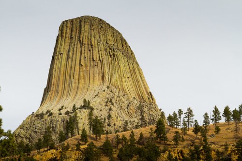 A towering rock formation with vertical stripes, surrounded by trees and a clear sky.