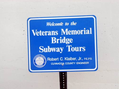 Blue sign welcoming visitors to the Veterans Memorial Bridge Subway Tours, featuring the name of the county engineer.