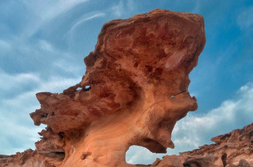 A large, uniquely shaped rock formation against a blue sky with wispy clouds.