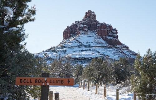 A snowy landscape with a sign for Bell Rock Climb, featuring a prominent red rock formation in the background.