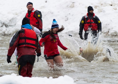 A woman in a red shirt and winter hat splashes through icy water, while others in rescue gear assist nearby.