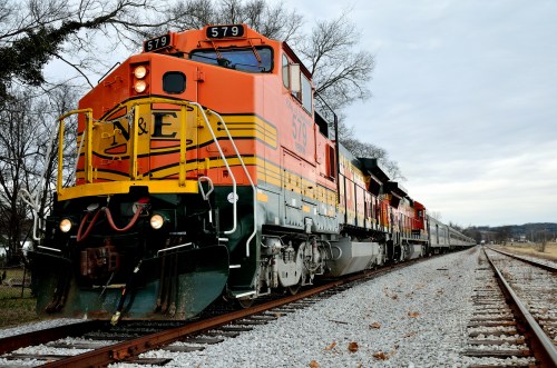 A colorful freight train with engine number 579 on tracks, surrounded by trees under a cloudy sky.