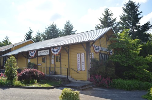 A yellow building with a metal roof, decorated with bunting, surrounded by greenery and trees.