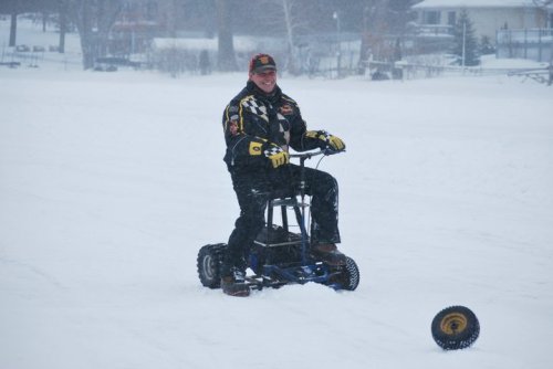 A person in winter gear rides a snow bike on a snowy landscape, smiling amid falling snowflakes.