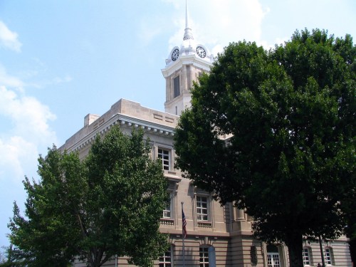 Historic building with a clock tower, surrounded by green trees and a clear blue sky.