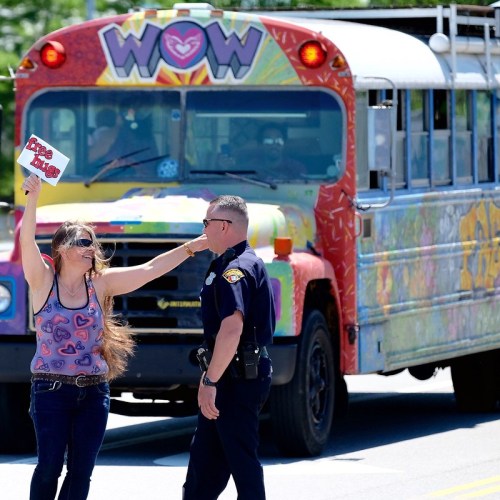 A woman holds a sign while interacting with a police officer near a colorful bus.